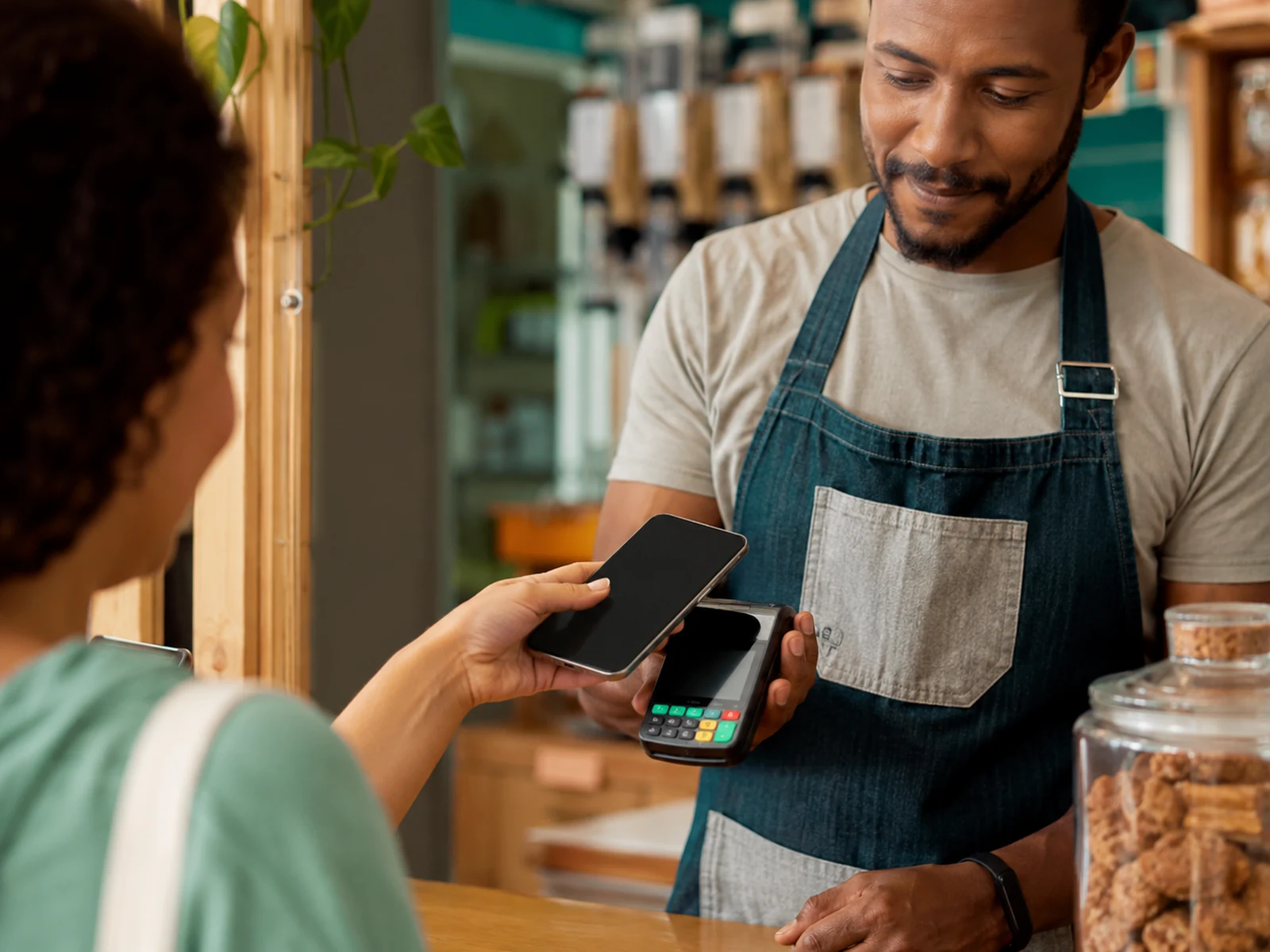 Cliente aproximando um celular de um terminal de pagamento em um pequeno negócio